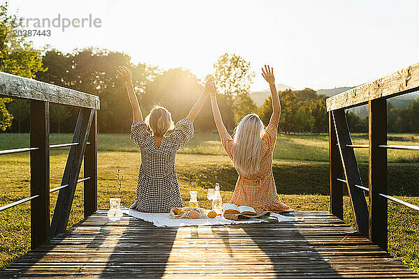 Friends with arms raised sitting on boardwalk in park