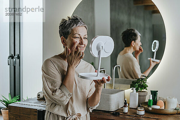 Smiling woman examining skin looking in mirror at home