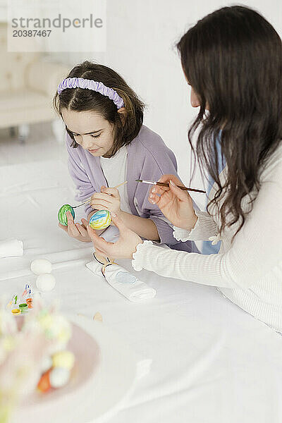 Woman teaching daughter to paint Easter eggs at home