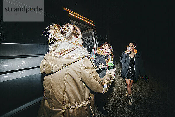 Women celebrating New Year's eve with champagne bottle near motor home at night