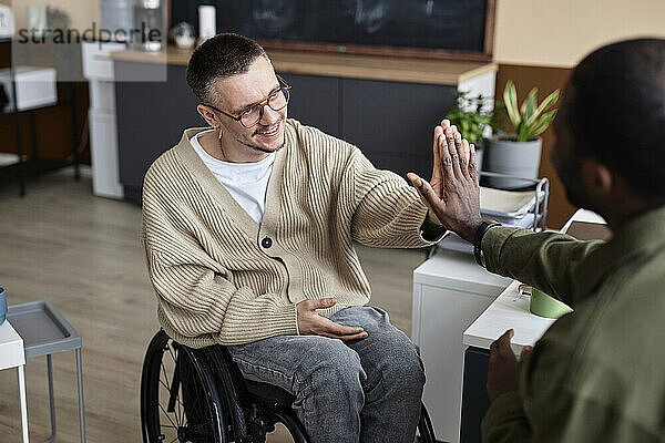Happy businessman with disability giving high-five to colleague in office