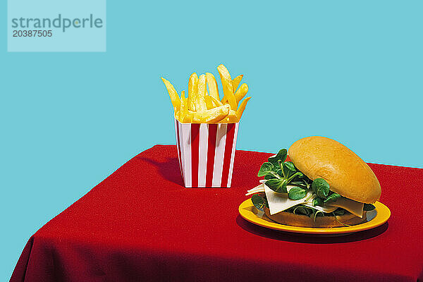 Chicken burger with french fries on table against blue background