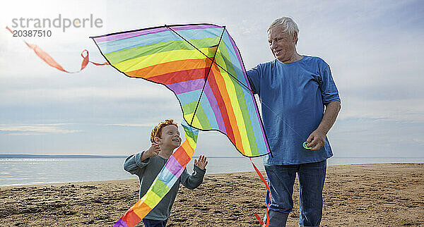 Senior man teaching grandson to fly kite at beach