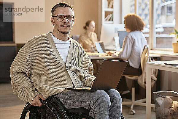 Businessman sitting with laptop in wheelchair at office