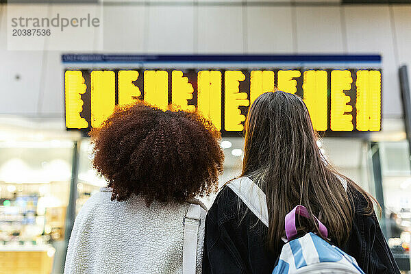 Friends looking at arrival departure board at railroad station lobby