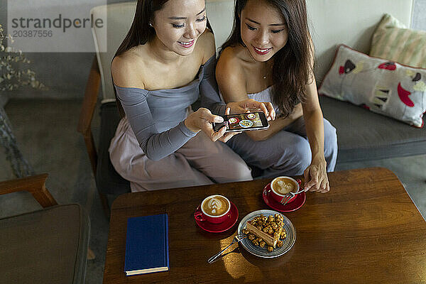 Smiling woman clicking photo of food through smart phone at restaurant