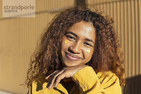 Happy beautiful young curly haired woman with yellow heart shape stickers on cheeks