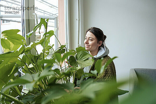 Smiling woman standing by plants near window day dreaming at home