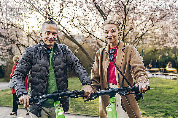 Smiling couple standing with electric push scooter on footpath