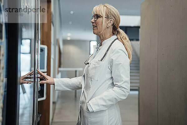 Smiling mature doctor standing in front of vending machine