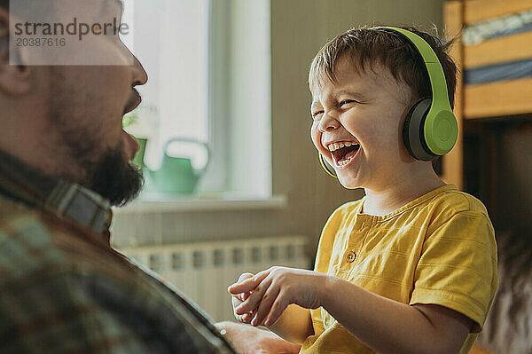 Cheerful boy listening to music through wireless headphones with father at home