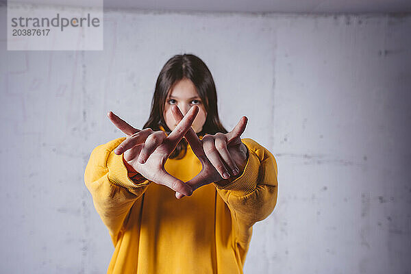 Girl in yellow hoodie gesturing in front of gray concrete background