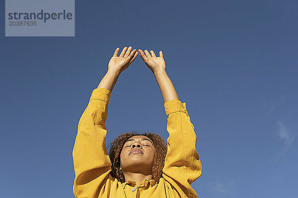Young woman with arms raised and eyes closed on sunny day