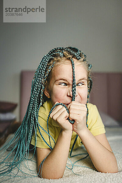 Girl playing with turquoise dyed braided hair lying on bed at home