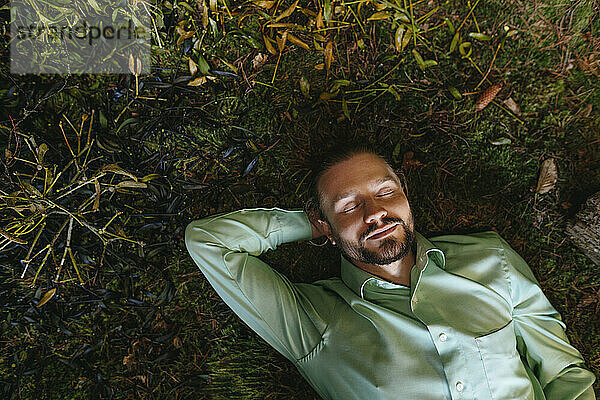 Businessman with eyes closed relaxing on moss