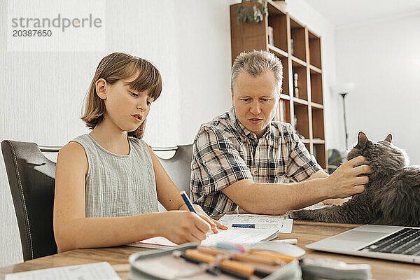 Man petting cat and helping daughter doing homework at home