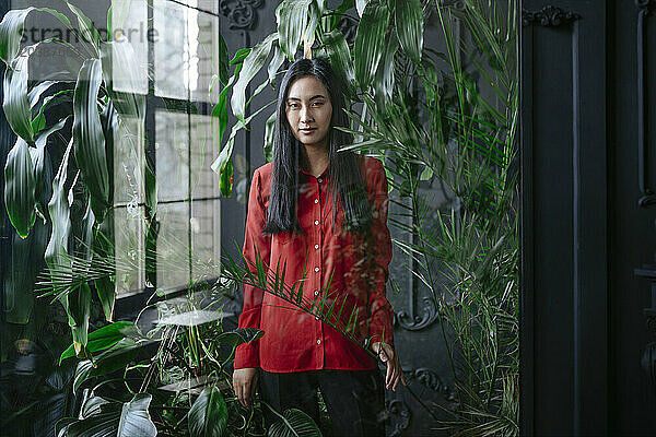Young woman standing near plants seen through glass