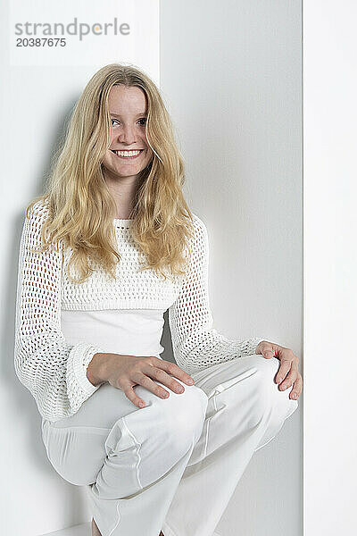 Smiling teenage girl squatting against white background