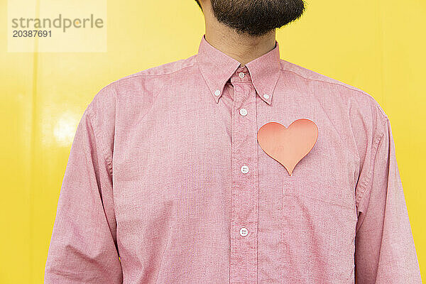 Man with heart over pink shirt against yellow background