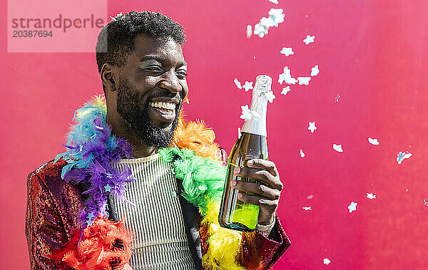 Cheerful non-binary person celebrating with champagne bottle against pink background