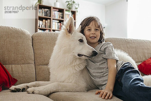 Smiling boy sitting with dog on sofa at home