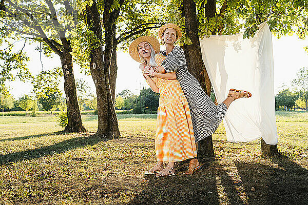 Happy woman carrying friend on piggyback in park