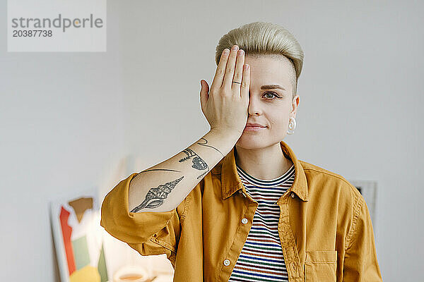 Woman covering eye with hand near white wall