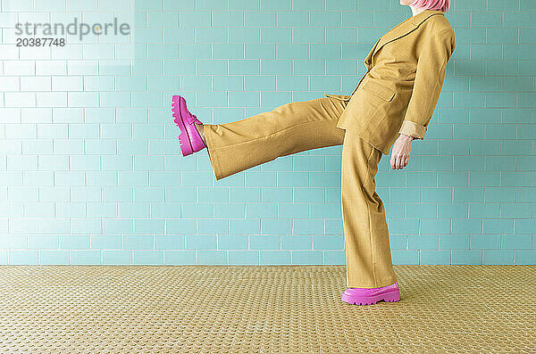 Woman standing on one leg near turquoise tile wall