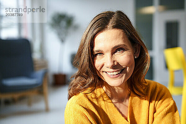 Happy mature woman under sunlight in living room at home