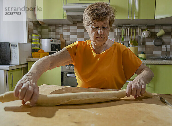 Senior woman rolling dough at table in kitchen at home