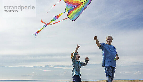 Elderly man flying kite with grandson at beach