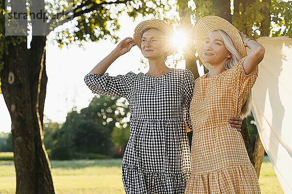 Contemplative women with hats standing in park