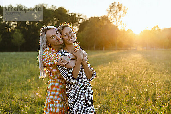 Happy friends embracing standing on grass in park