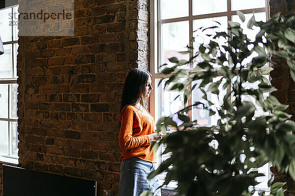 Young woman leaning on wall and looking out of window at cafe