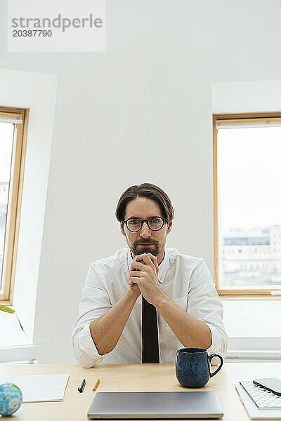 Businessman sitting with laptop and coffee cup at desk in window