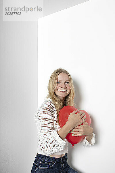 Smiling teenage girl with heart shape balloon against white background
