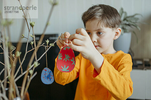 Boy decorating cardboard Easter eggs on twig at home