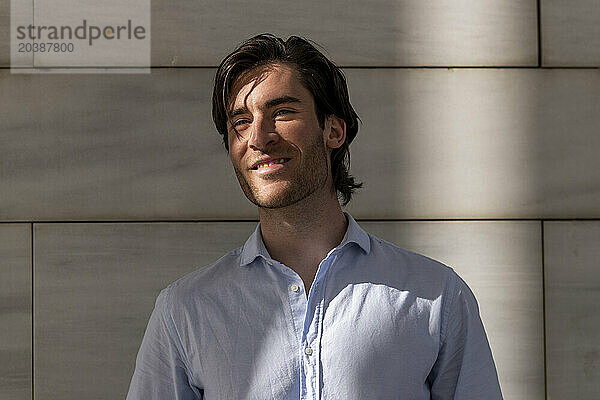 Smiling young businessman in front of wall