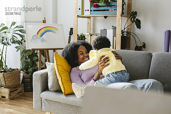 Happy single mother lying on sofa playing with baby girl in living room at home