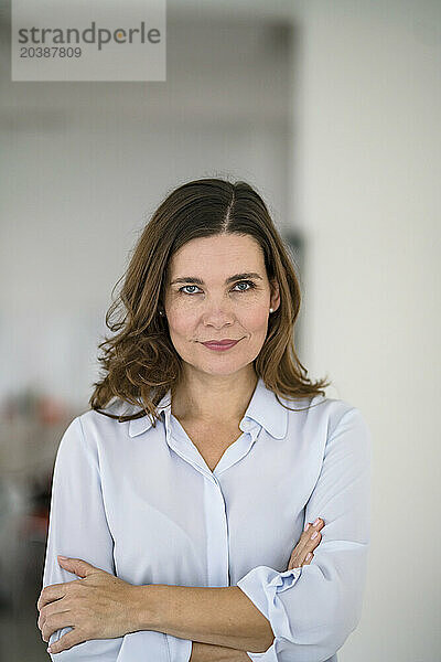 Confident businesswoman with arms crossed in creative office