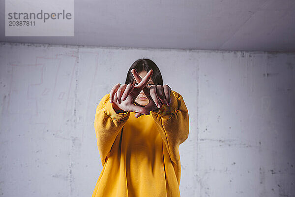 Girl in yellow hoodie gesturing in front of gray background