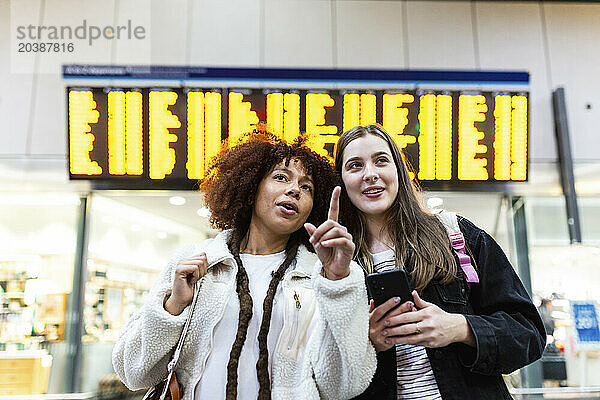 Woman gesturing with friend standing at railroad station