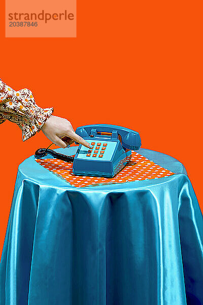 Hand of woman dialing on keypad of telephone against orange background