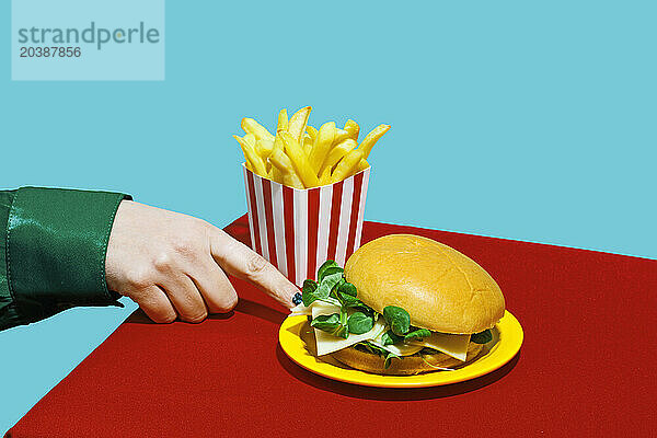 Hand of woman touching plate of cheeseburger on table against blue background