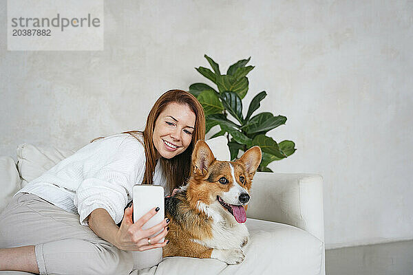 Happy woman taking selfie with dog on couch at home