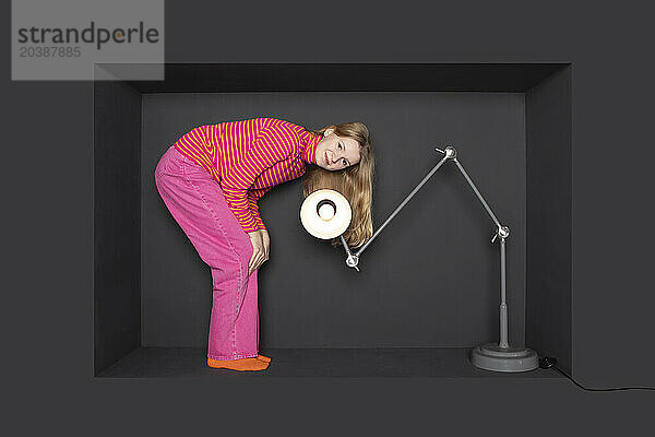 Smiling blond girl standing by electric lamp