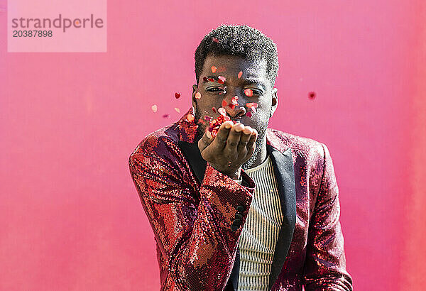 Young non-binary person blowing confetti against pink background