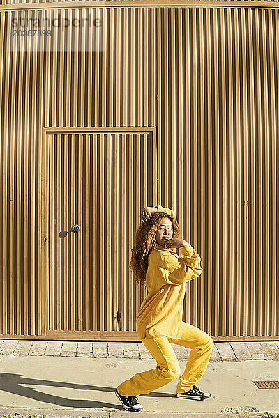 Woman wearing yellow casuals dancing in front of metal wall on sunny day