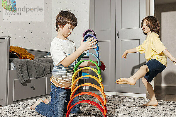 Happy boy with brother building pyramid with colorful rainbow toys at home