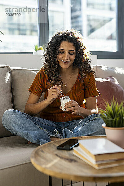 Smiling woman having yogurt on sofa at home